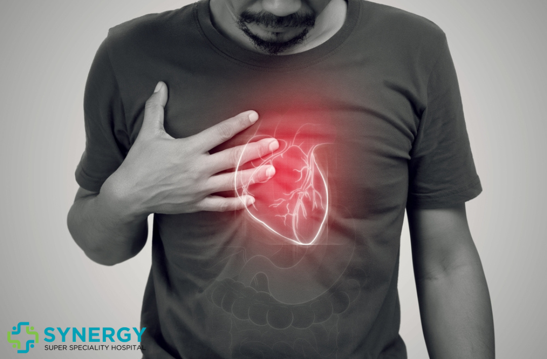 A man clutching his chest with a glowing red area symbolizing heart pain, representing heart-related health issues, accompanied by the Synergy Super Speciality Hospital logo.