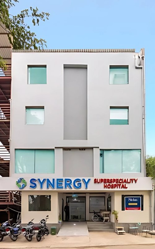 Front view of the Synergy Super Speciality Hospital building in Bhopal, showing a modern multi-story structure with glass windows, clean architecture, and the hospital logo and signage above the entrance.