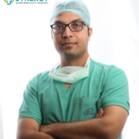 A confident doctor in surgical scrubs and cap, with arms crossed, representing Synergy Super Speciality Hospital.