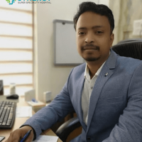 A professional male doctor at Synergy Super Speciality Hospital, seated at his desk, wearing a light blue blazer and white shirt, representing expertise and care.
