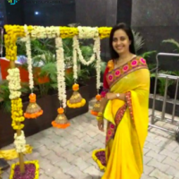 A woman in a yellow saree standing near a floral arch during a festive event at Synergy Super Speciality Hospital in Bhopal.